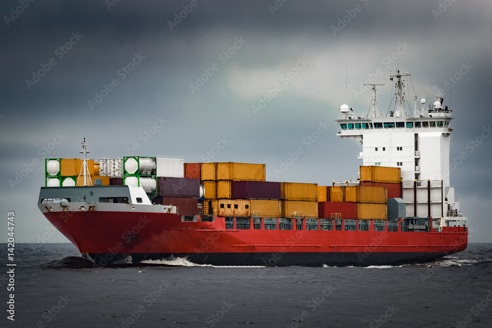 Fototapeta premium Red cargo container ship sailing from Baltic sea in cloudy day
