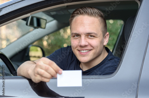 Young man leaning from a car showing his licence