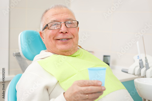 Closeup portrait of Smile Old senior man with plastic cup sitting in a chair in dental clinic. Looking to camera