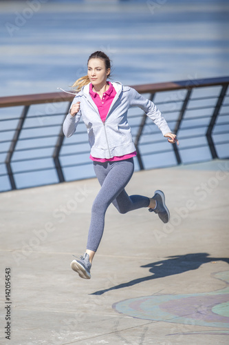 Morning exercise near the river. Young woman on recreation and jogging.