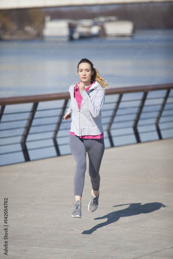 Obraz premium Morning exercise near the river. Young woman on recreation and jogging.