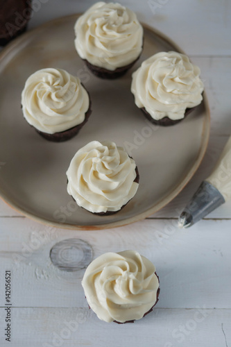 chocolate muffins and cupcakes white cream beige ceramic plate on white wooden table close-up top view