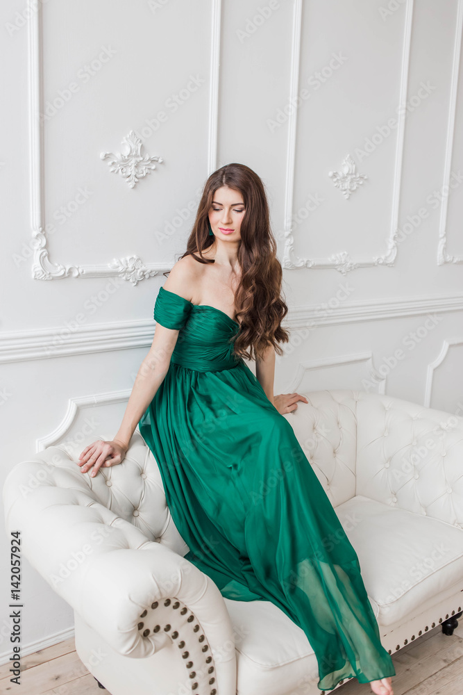 beautiful girl in the emerald green dress brunette with long wavy hair on a  white background sitting on a leather couch looking down Stock-Foto | Adobe  Stock