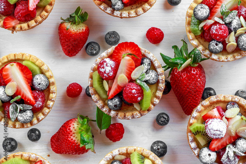 Berry tartlets with blueberries, raspberries, kiwi, strawberries, almond flakes in icing sugar Fototapet
