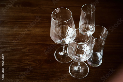Empty clean glasses for champagne, cocktails, wine and water stand on a textured wooden table in the interior of the restaurant