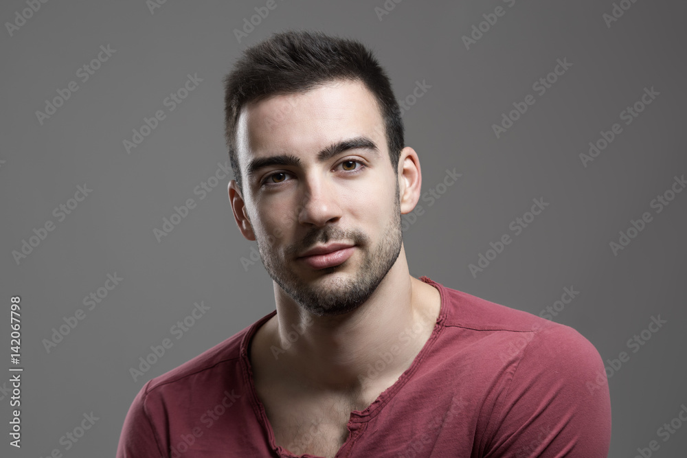 Cool handsome male fashion model in red v-neck shirt looking at camera. Atmospheric contrasty portrait over gray studio background. Cool handsome male fashion model in red v-neck shirt looking at camera. Atmospheric contrasty portrait over gray studio background.