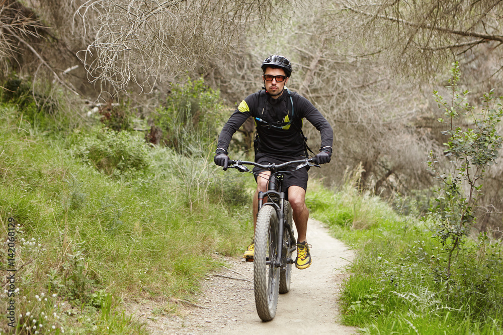 Fototapeta premium Confident professional rider preparing for cycling contest riding his electric bike, using pedal-assist system. Confident young European biker enjoying freeride outdoors in woods in the morning