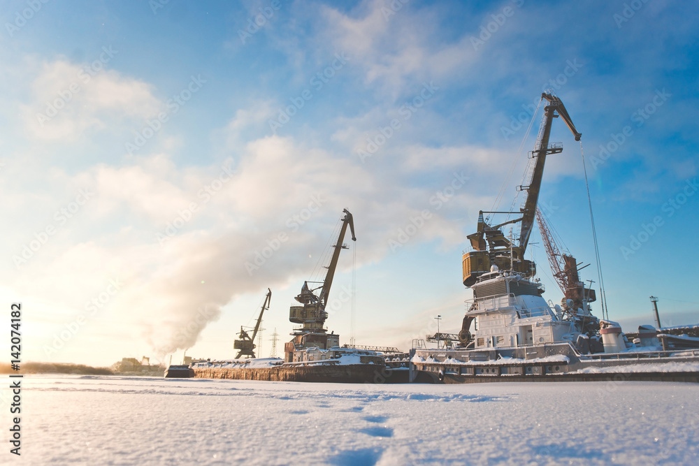 Ships cargo cranes on shore in winter at sunset.