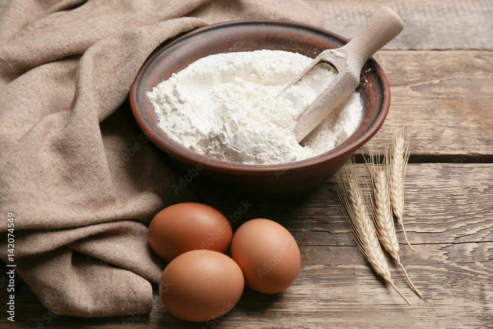 Bowl with flour, eggs and scoop on wooden table Bowl with flour, eggs and scoop on wooden table