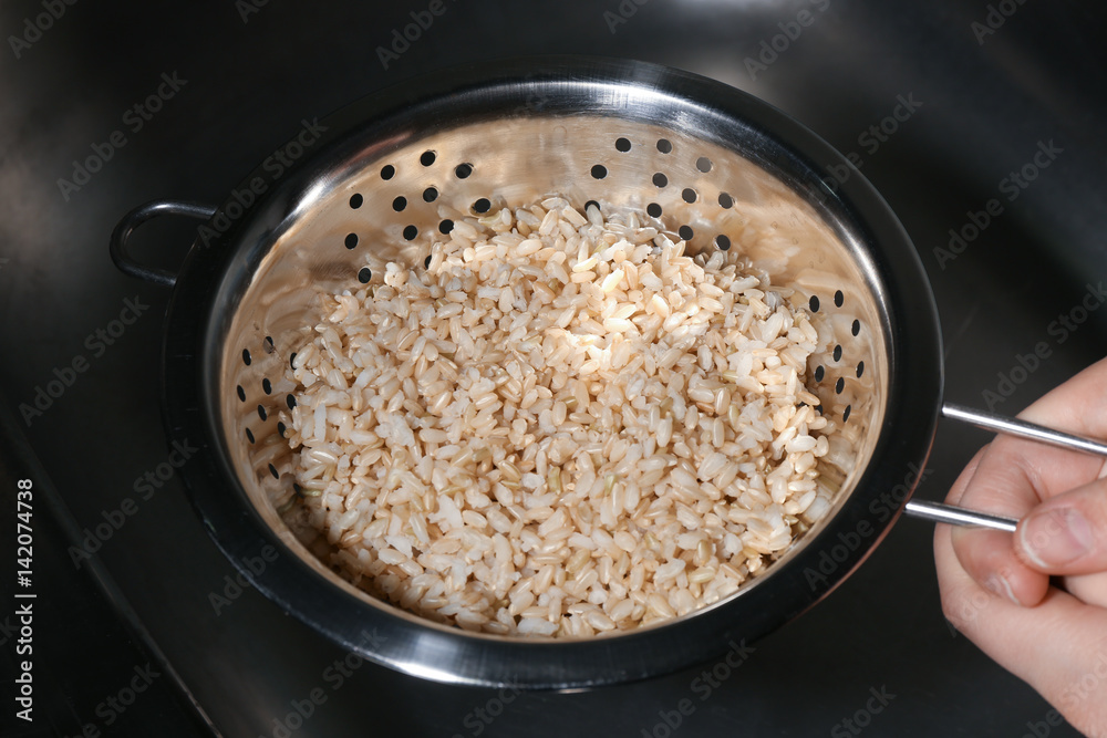 Female hand holding colander with brown rice Female hand holding colander with brown rice