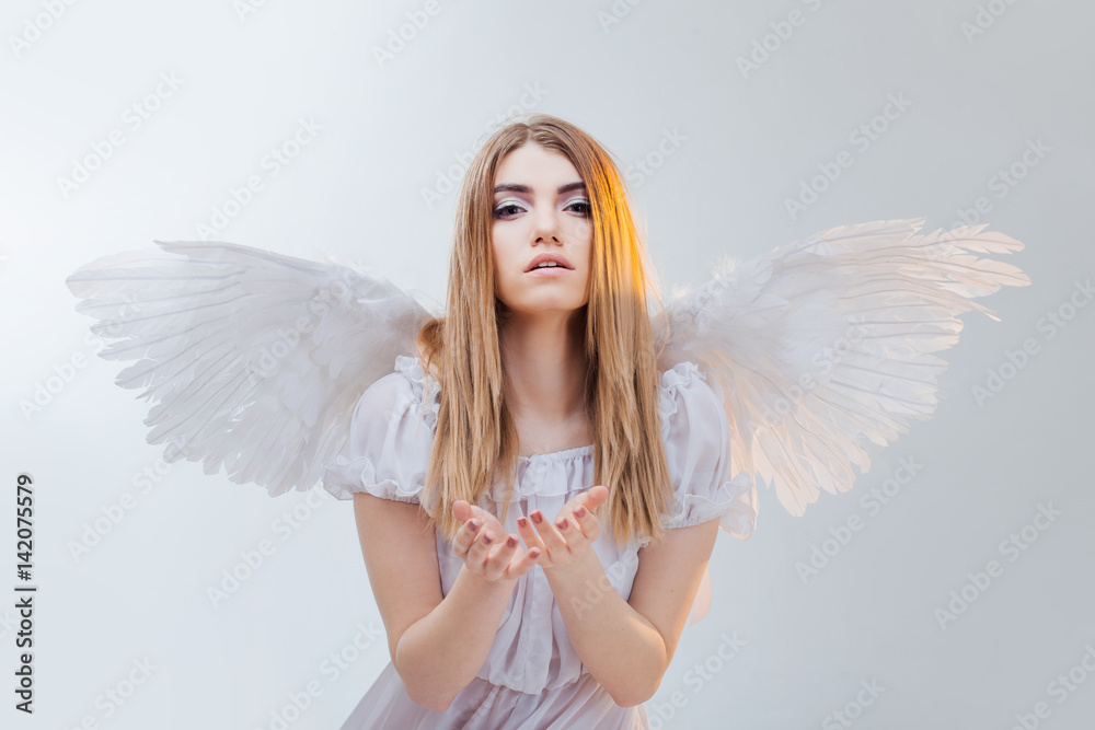 An angel from heaven holding something on the palms. Young, wonderful blonde girl in the image of an angel with white wings. An angel from heaven holding something on the palms. Young, wonderful blonde girl in the image of an angel with white wings.