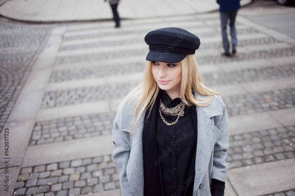 Young, hip and attractive blonde walking around the city, girl in a stylish hat and a gray coat. Pedestrian crossing Young, hip and attractive blonde walking around the city, girl in a stylish hat and a gray coat. Pedestrian crossing