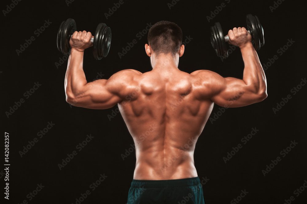 Muscular male model bodybuilder doing exercises with dumbbells, turned back. Isolated on black background with copyspace