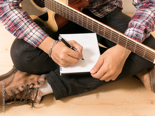 Young hipster composing the song with guitar .