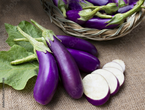 Raw violet eggplant in a wicker basket on sackcloth.
