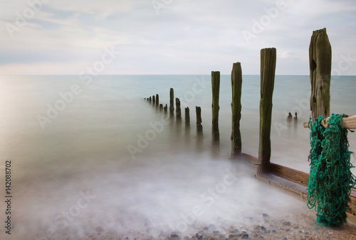 Long-exposure seascape of wooden sea defences and milky calm sea and cloud.