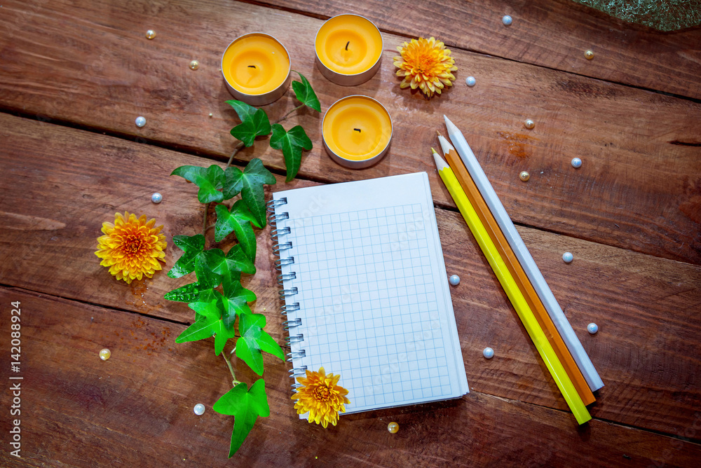 Blank spiral notepad, colorful pencils, orange aroma candles, aster flowers and ivy branch with water drops on wooden background. Space for text or massage.