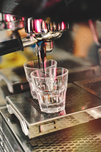 Professional coffee brewing. Coffee espresso. Close-up of espresso pouring from coffee machine to shotglasses. photo