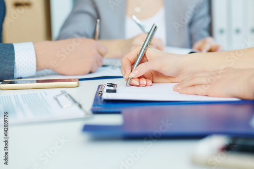 Business woman making notes at office workplace with colleague on the background. Business job offer, financial success, certified public accountant concept.