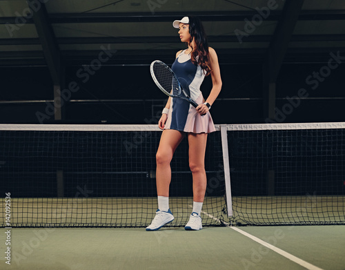 Female tennis player posing on an indoor tennis court. © Fxquadro