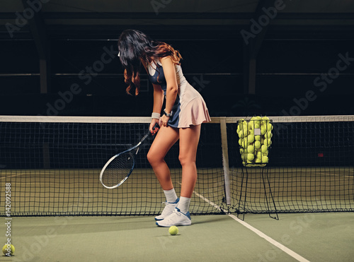 Female tennis player posing on an indoor tennis court. © Fxquadro