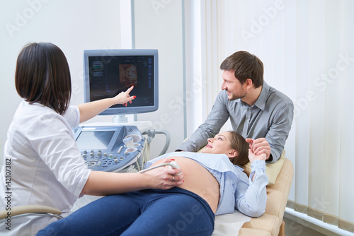 Fototapeta Loving couple attending doctor for pregnancy ultra sound procedu