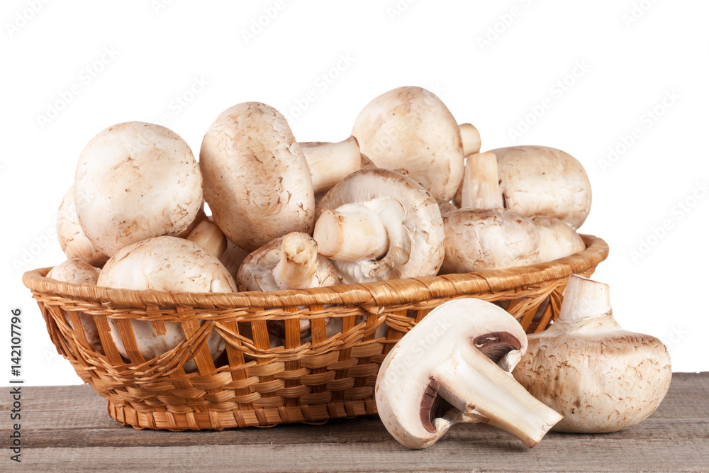 Champignon mushrooms in a wicker basket on a wooden table with white background Champignon mushrooms in a wicker basket on a wooden table with white background