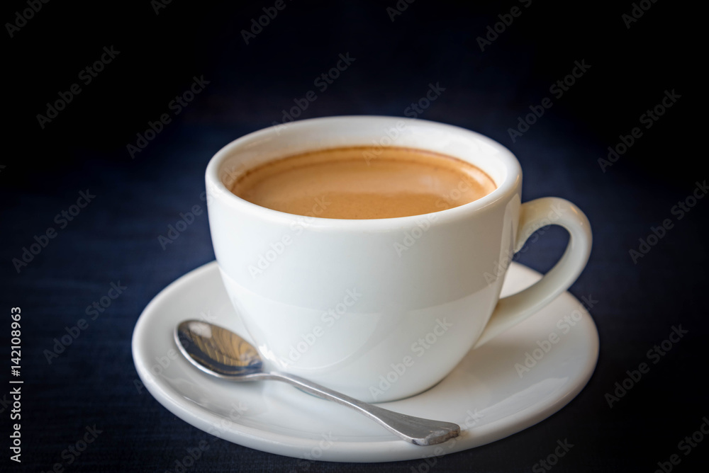 White cup of coffee on dark blue background White cup of coffee on dark blue background