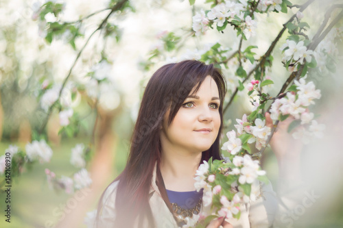 beautiful young brunette woman standing near the blossoming apple tree on a warm spring day