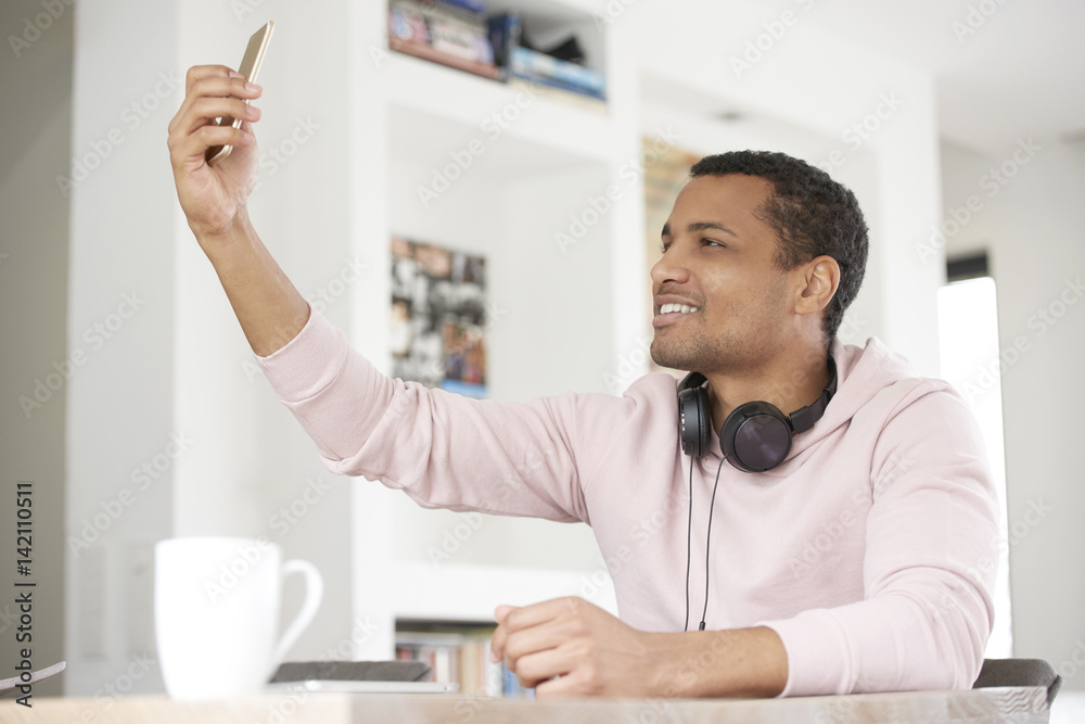 Take a selfie. Cropped shot of a handsome Afro American young man using his cellphone and taking selfie while chilling at home.