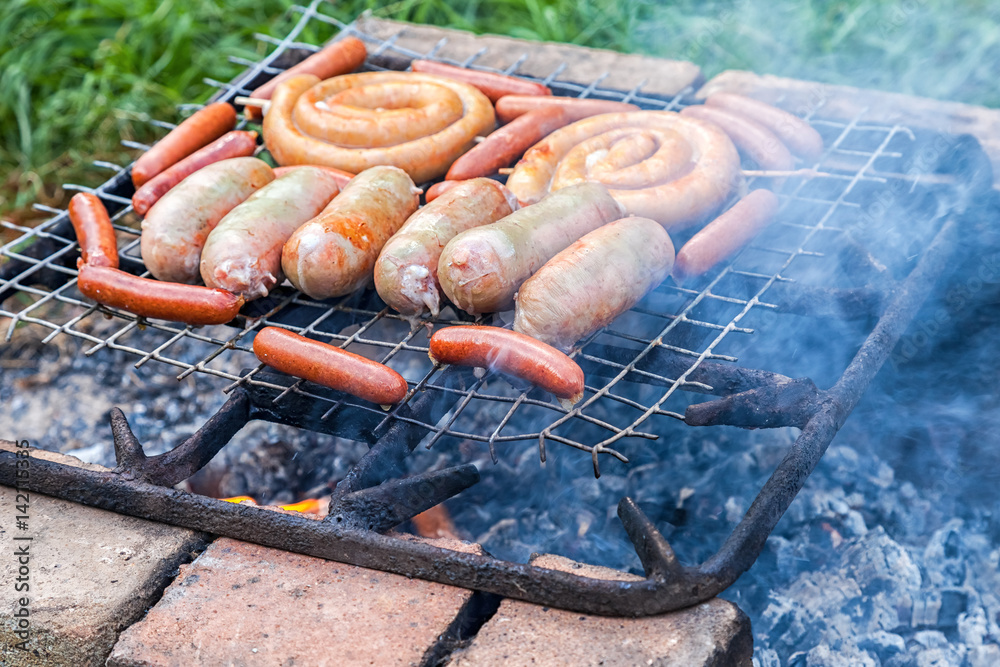 Tasty pork and beef sausages cooking over the hot coals on a barbecue fire