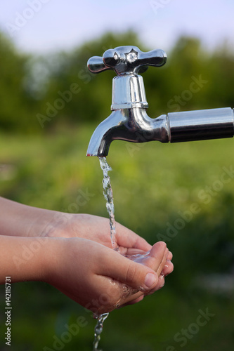 boy washes his hand under the faucet in garden