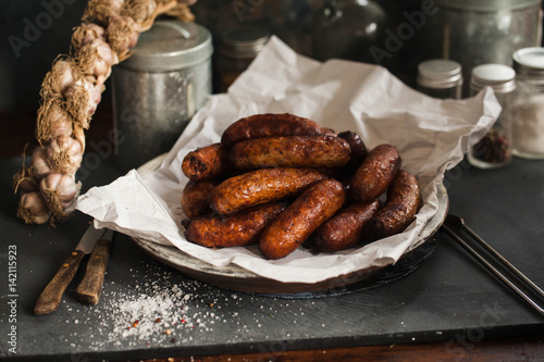 Bunch OF Fried Sausages on Plate Over White Paper WIth Garlic Braid And Spcies' Containers photo