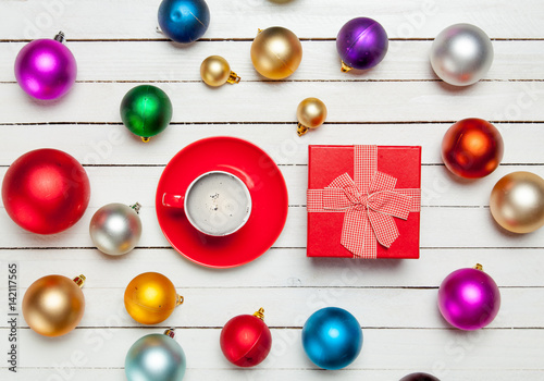 photo of red cup of coffee and cute gift near colorful baubles on the wonderful white wooden background