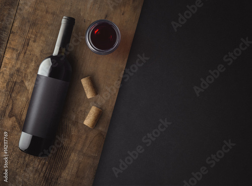 Bottle of red wine with label on old board. Glass of wine and cork. Wine bottle mockup. Top view.