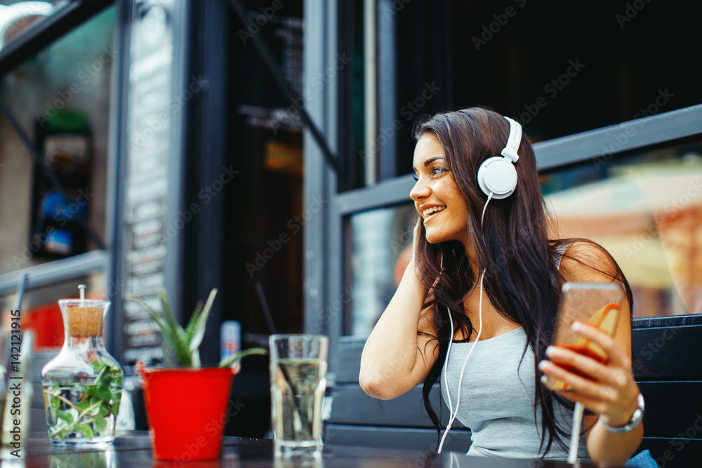 Fototapeta premium Beautiful young woman listening to music in sidewalk cafe via headphones