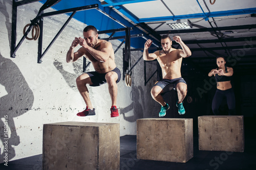 Group of athletic people jumpin over some boxes in a cross-training gym photo
