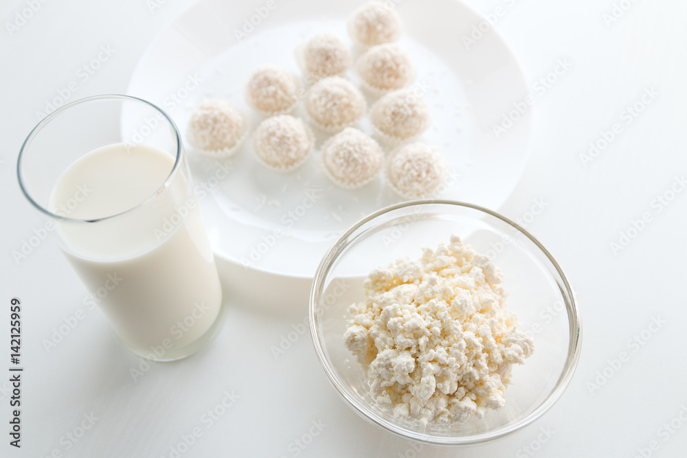 Raffaello candy in baskets on a plate, with milk in a glass and jug, cottage cheese in a bowl in the background, on a white table, in a high key, with space for text Raffaello candy in baskets on a plate, with milk in a glass and jug, cottage cheese in a bowl in the background, on a white table, in a high key, with space for text