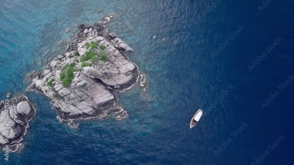 Aerial top view shot of a rocky tropical island and a scuba diving boat next to it. Snorkelers, divers, and kayakers on clear blue waters.