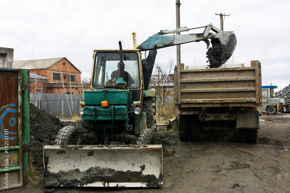 An old Soviet tractor digs and loads waste stone processing near the shop