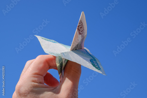 Denominations of Russian money, folded in the airplane against the blue sky in hand