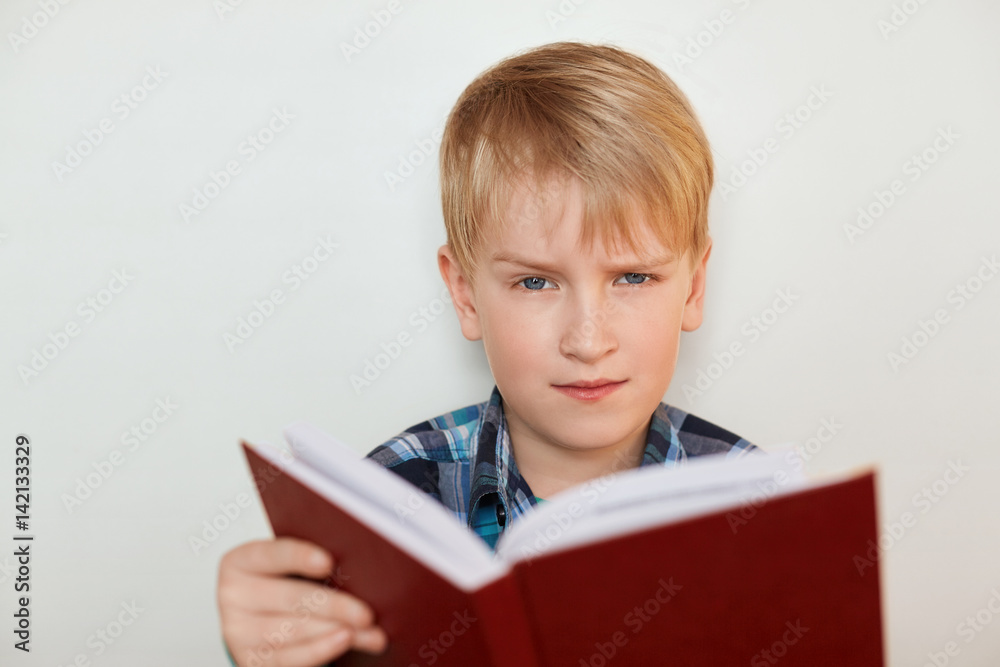 Human face expressions and emotions. Children and education. A close-up of attractive little boy with fair hair reading a book being tired of homework having angry expression. Boring school studies Human face expressions and emotions. Children and education. A close-up of attractive little boy with fair hair reading a book being tired of homework having angry expression. Boring school studies