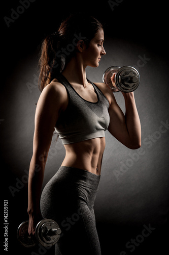 Atractive fit woman works out with dumbbells as a fitness conceptual over dark background