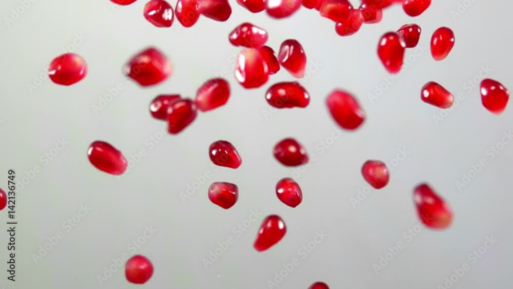 Red ripe garnet seeds fly on a white background in slow motion Red ripe garnet seeds fly on a white background in slow motion