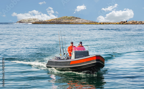 Two fishermen sail on a motor boat by sea against the background of the island. Float directly to the camera