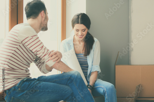 Young couple sitting on the floor and looking at the blueprint of new home