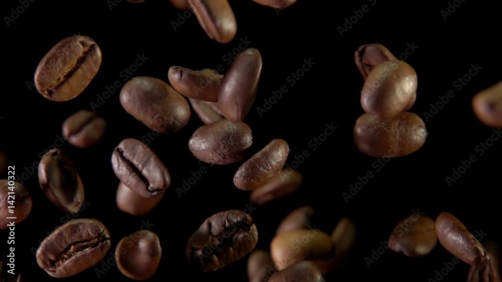 Fried coffee beans fly to the camera on a dark background. Slow-motion shooting, very close-up