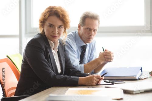 Business concept. Angry boss woman looking at camera while sitting in board room with her colleagues or workers in office. People negotiating.