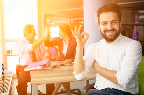Interview concept. Toned of bearded man looking at camera, smiling and showing okay sign. Young businessman looking happy after successful interview to huge company.