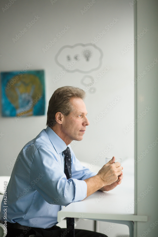 Handsome confident man looking at window and having rest. Businessman having coffee break during his work in office.